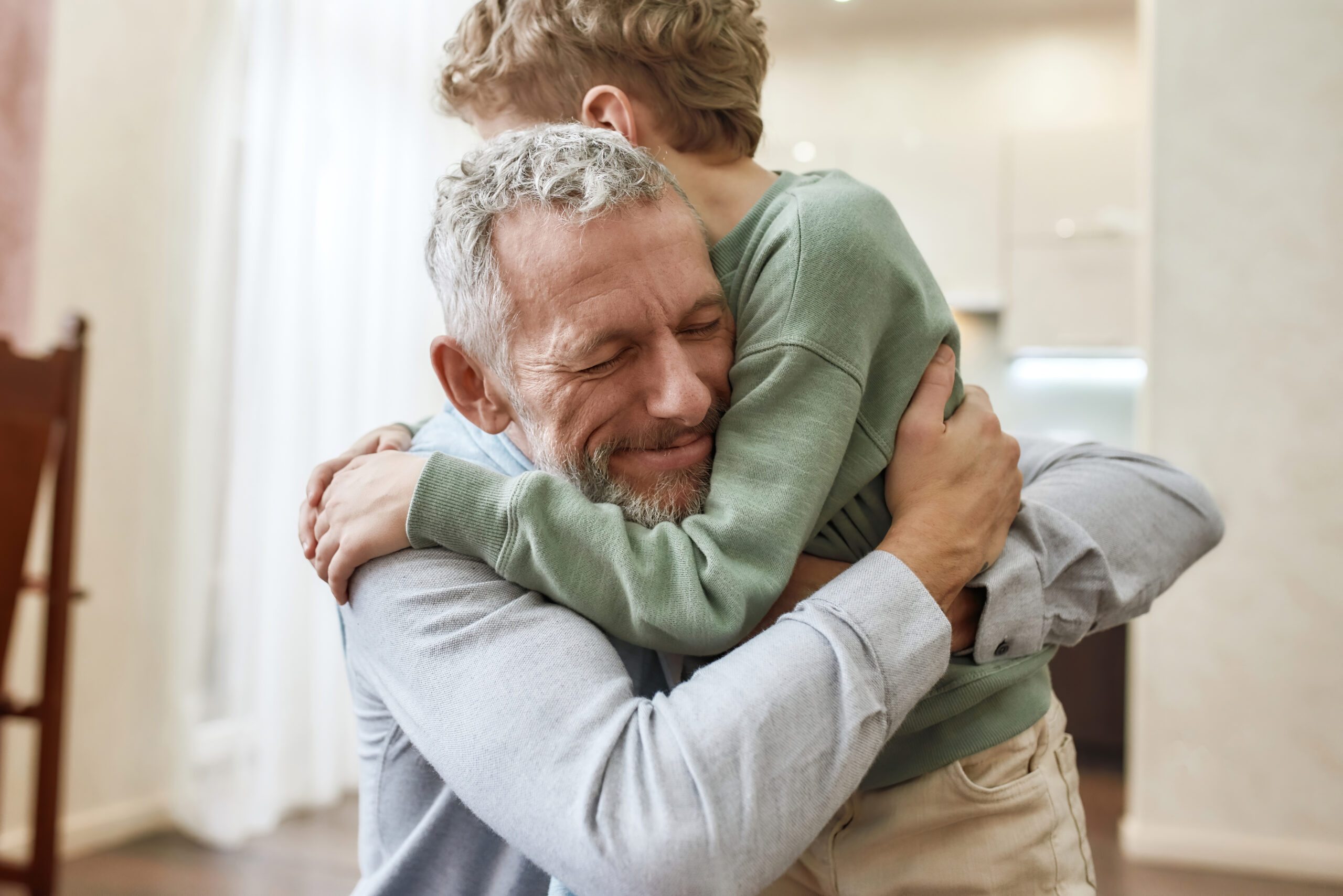 Emotional meeting. Happy grandfather embracing his cute little preschool grandson while standing together at home
